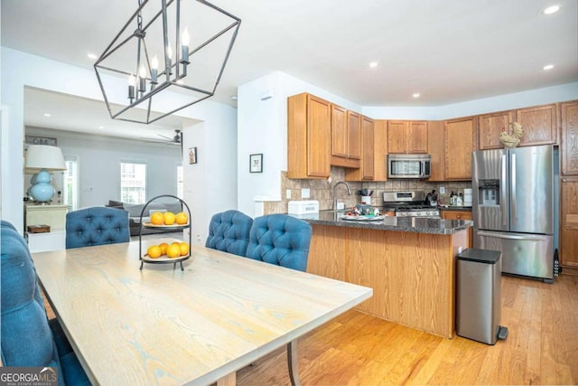 kitchen featuring a sink, backsplash, a peninsula, light wood-style flooring, and stainless steel appliances