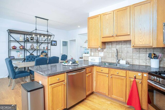 kitchen with a sink, a peninsula, light wood-style flooring, stainless steel appliances, and decorative backsplash