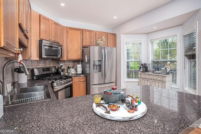 kitchen with stainless steel appliances, backsplash, a sink, a peninsula, and brown cabinetry