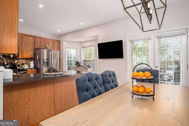 kitchen featuring backsplash, stainless steel fridge, dark stone countertops, open floor plan, and brown cabinetry