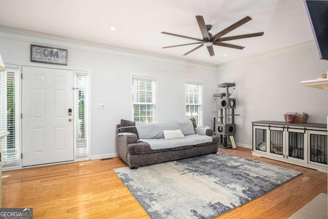 living room featuring a ceiling fan, crown molding, baseboards, and wood finished floors