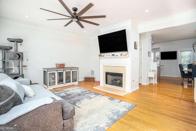living room featuring baseboards, ornamental molding, wood finished floors, a fireplace with raised hearth, and a ceiling fan
