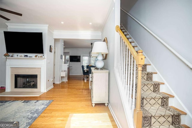 stairs with a ceiling fan, wood finished floors, a fireplace with raised hearth, baseboards, and ornamental molding