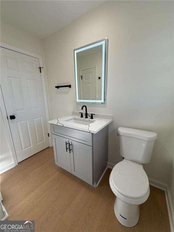half bath with toilet, wood finished floors, baseboards, and vanity