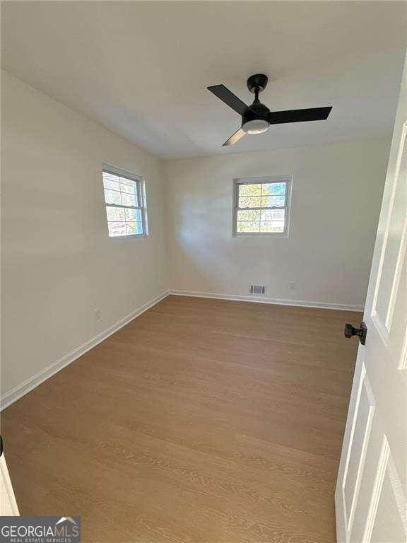 spare room featuring a ceiling fan, visible vents, baseboards, and wood finished floors