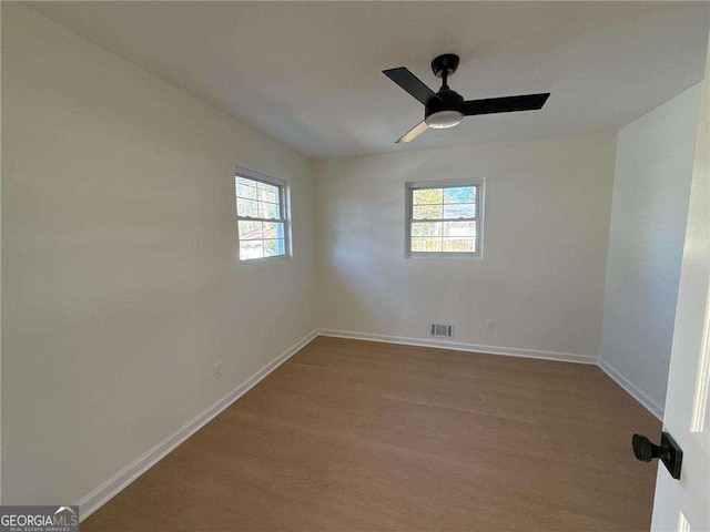 spare room featuring wood finished floors, baseboards, ceiling fan, and visible vents