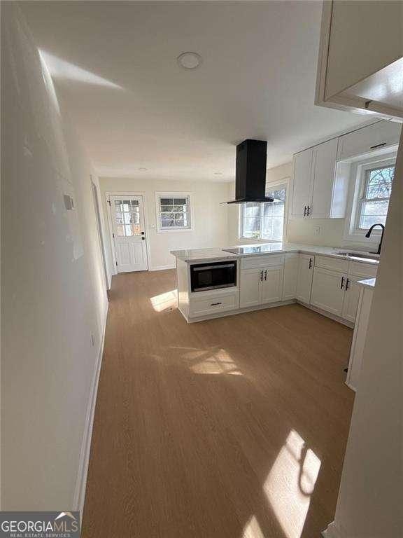 kitchen with a sink, light wood finished floors, built in microwave, island exhaust hood, and white cabinets