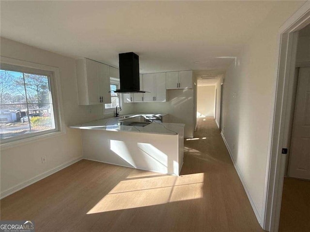 kitchen with white cabinets, island exhaust hood, a peninsula, wood finished floors, and a sink