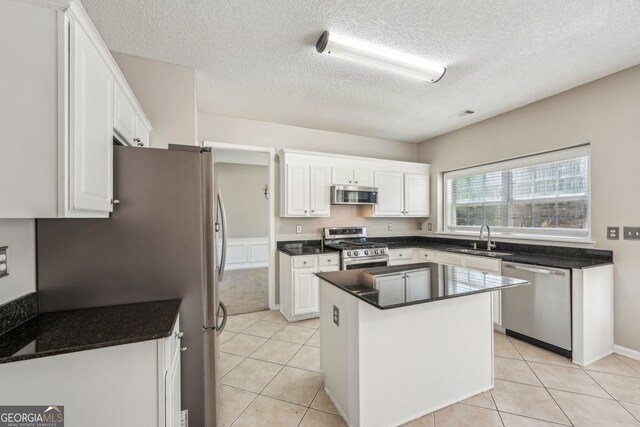 3936 Toccoa Falls Dr, Duluth, GA 30097 - kitchen featuring appliances with stainless steel finishes, a sink, white cabinetry, a textured ceiling, and a kitchen island