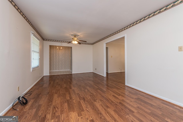 empty room with ornamental molding, ceiling fan, wood finished floors, and baseboards