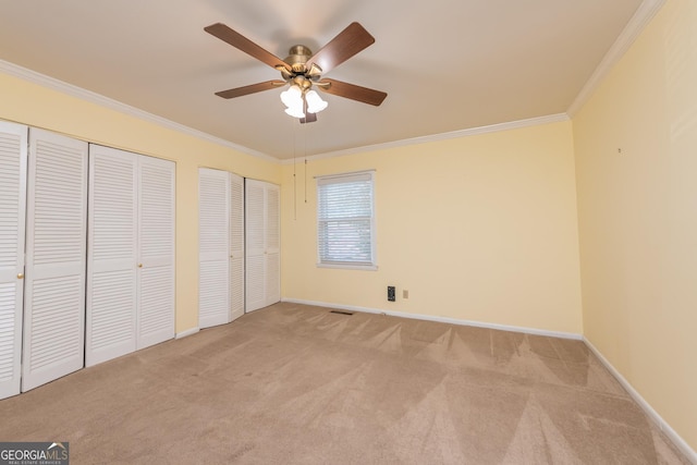 unfurnished bedroom with ornamental molding, multiple closets, and light colored carpet