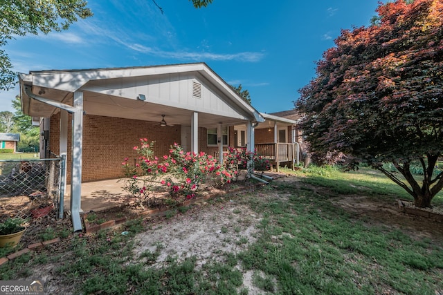 back of property featuring a carport, a ceiling fan, brick siding, a lawn, and covered porch
