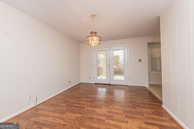 unfurnished dining area featuring baseboards, a notable chandelier, crown molding, wood finished floors, and french doors