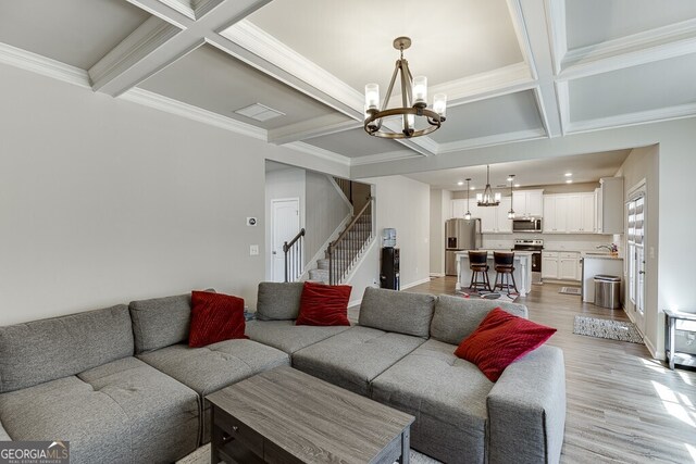 living room with coffered ceiling, stairway, a chandelier, light wood-style floors, and beamed ceiling
