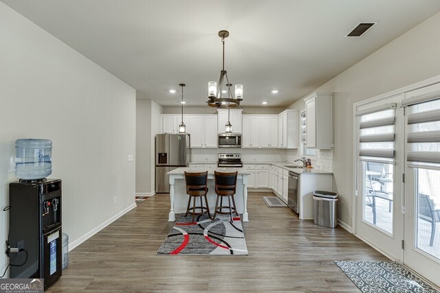 kitchen featuring light wood-type flooring, stainless steel appliances, visible vents, white cabinets, and decorative backsplash