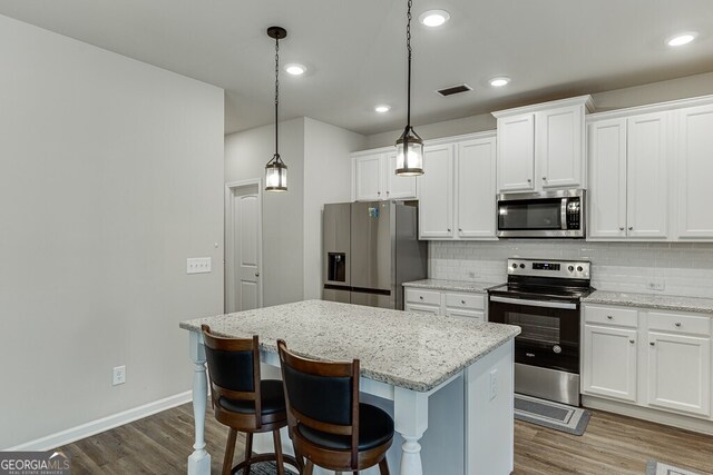 kitchen with visible vents, stainless steel appliances, a kitchen island, tasteful backsplash, and dark wood-style floors