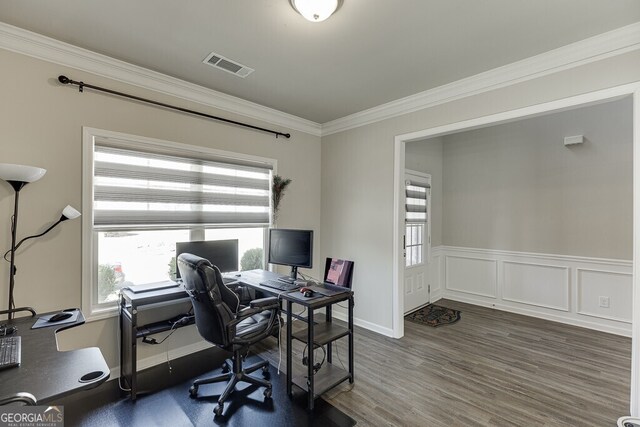 home office featuring wood finished floors, ornamental molding, visible vents, a decorative wall, and wainscoting