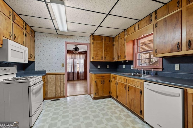 kitchen with white appliances, wallpapered walls, light floors, and a sink