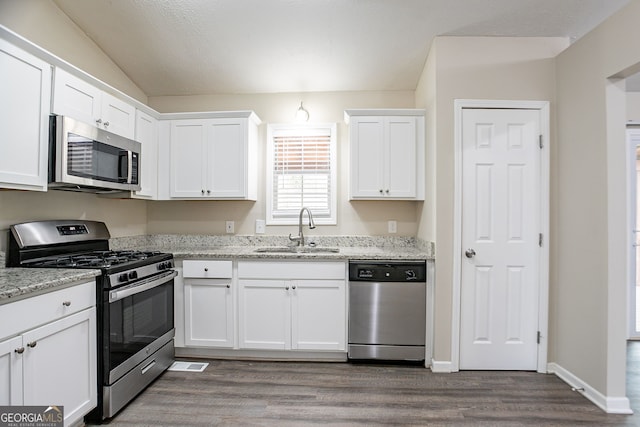 kitchen featuring dark wood-style flooring, stainless steel appliances, a sink, light stone counters, and white cabinets