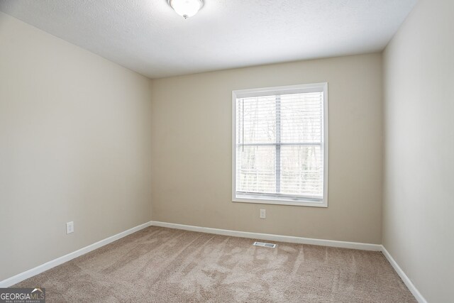 carpeted spare room with a textured ceiling, baseboards, and visible vents