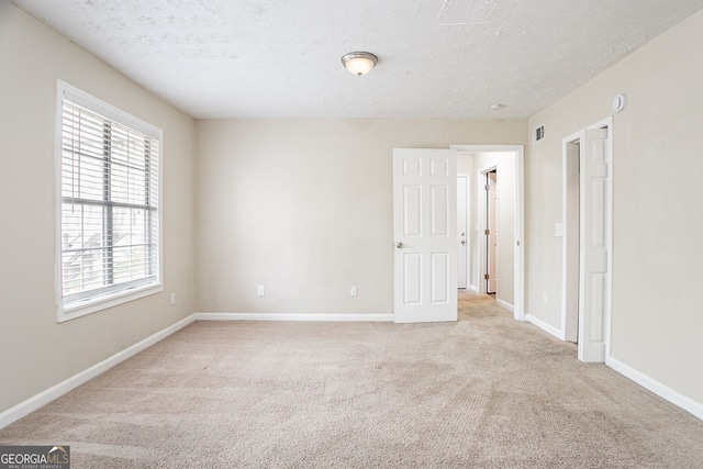 spare room with visible vents, baseboards, light colored carpet, and a textured ceiling