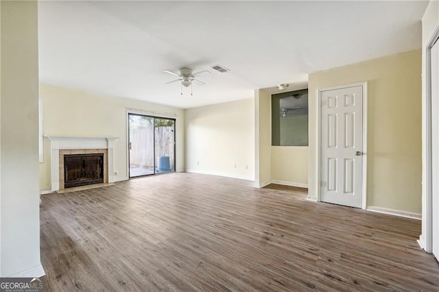 unfurnished living room with a tiled fireplace, a ceiling fan, baseboards, and wood finished floors