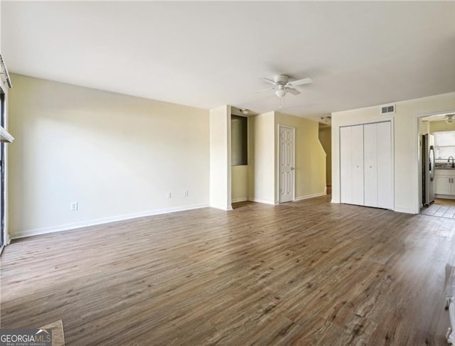 unfurnished living room with wood finished floors, visible vents, baseboards, and ceiling fan