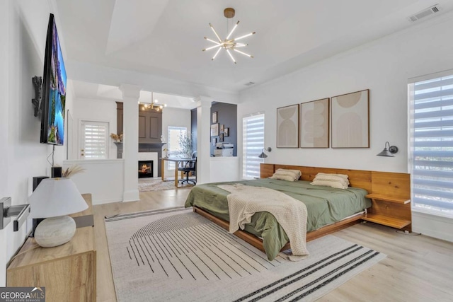 bedroom featuring visible vents, an inviting chandelier, a lit fireplace, and ornate columns