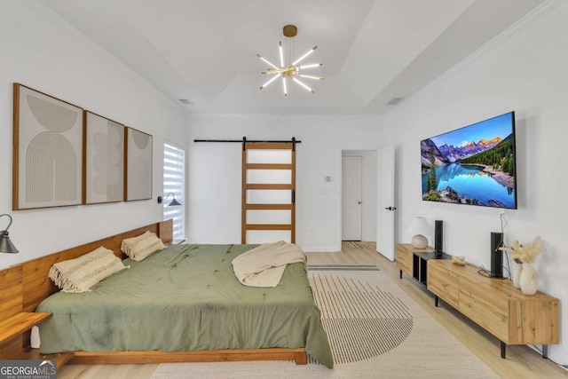 bedroom with light wood finished floors, a barn door, a chandelier, and a raised ceiling