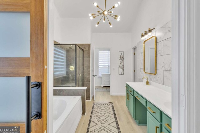 bathroom with a chandelier, a shower stall, a sink, a garden tub, and wood finished floors
