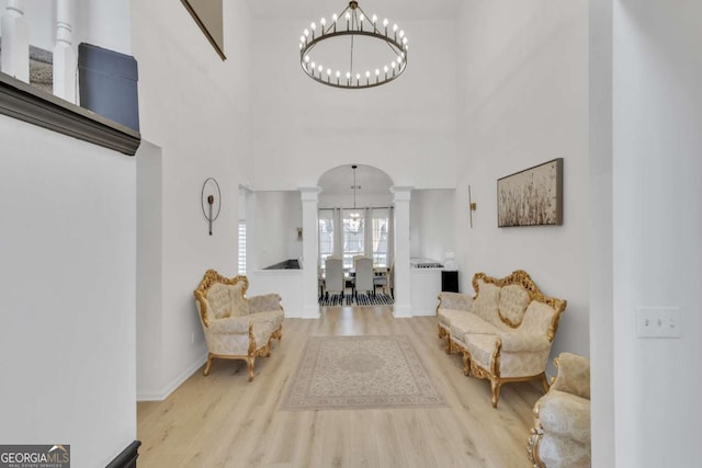 living area featuring wood finished floors, baseboards, ornate columns, a towering ceiling, and an inviting chandelier