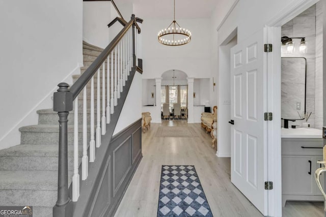 entryway with stairway, a chandelier, light wood-style flooring, arched walkways, and ornate columns