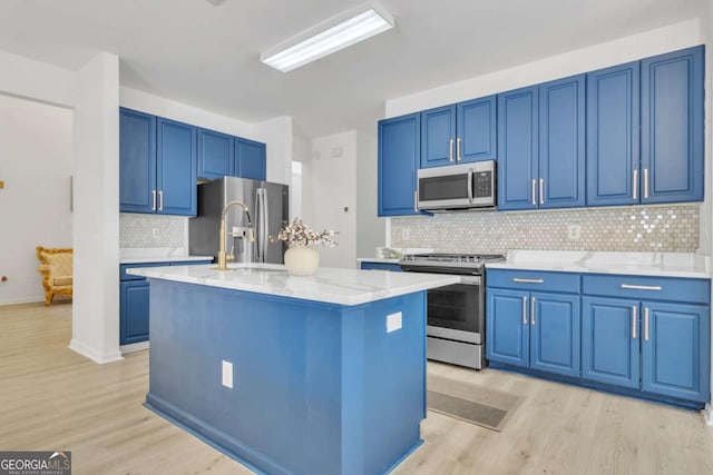 kitchen with light wood-style flooring, a kitchen island with sink, blue cabinets, and appliances with stainless steel finishes