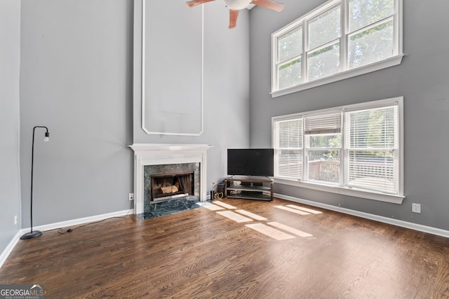 unfurnished living room featuring a towering ceiling, wood finished floors, a ceiling fan, baseboards, and a fireplace
