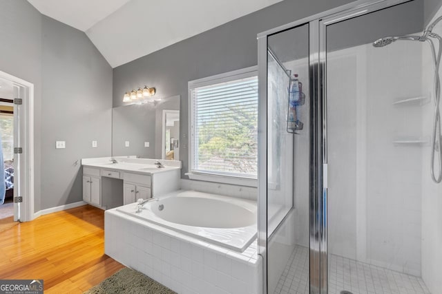 bathroom featuring a bath, double vanity, lofted ceiling, wood finished floors, and a shower stall
