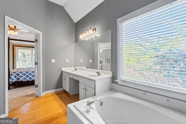 bathroom featuring wood finished floors, a sink, a bath, double vanity, and lofted ceiling