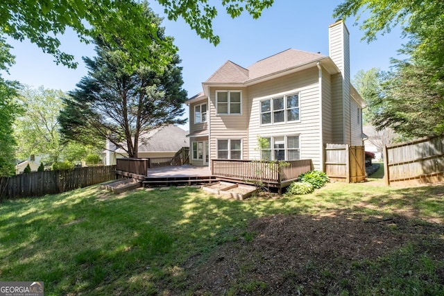 back of property featuring a wooden deck, a lawn, a chimney, and a fenced backyard