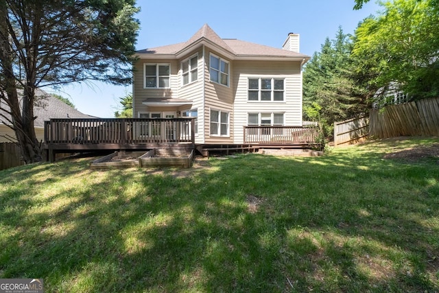 back of property with a yard, a chimney, fence, and a deck