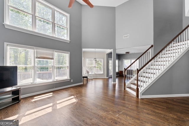 unfurnished living room with wood finished floors, stairs, a high ceiling, baseboards, and visible vents