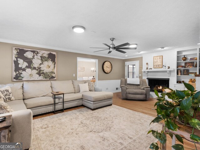 living area with ornamental molding, wood finished floors, a brick fireplace, and ceiling fan
