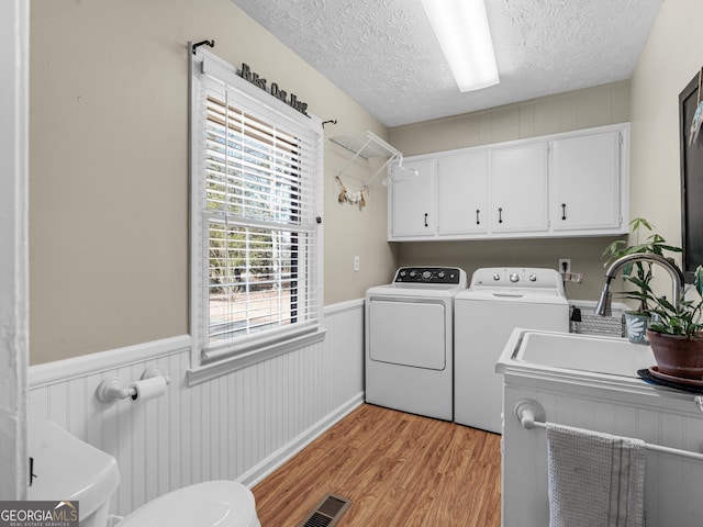laundry room featuring washer and clothes dryer, cabinet space, light wood-type flooring, a textured ceiling, and wainscoting