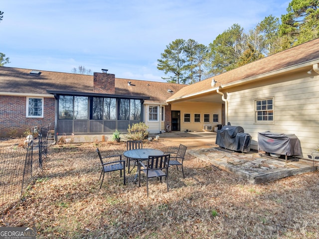 rear view of property featuring a chimney, a patio, a sunroom, a shingled roof, and brick siding
