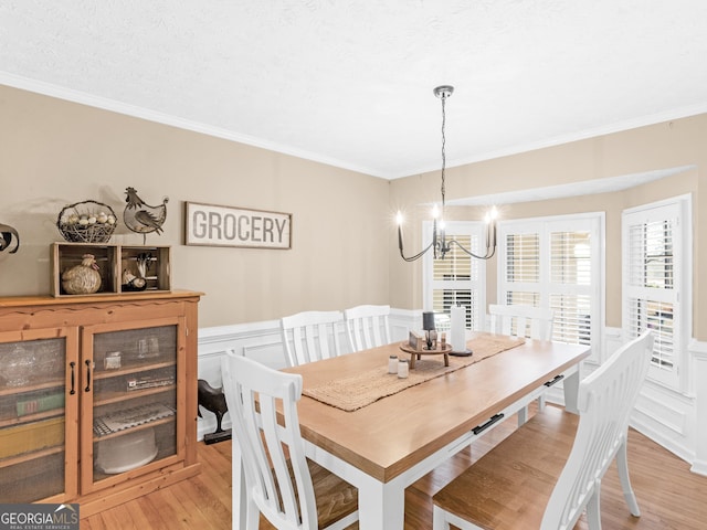 dining area featuring ornamental molding, a chandelier, light wood finished floors, wainscoting, and a decorative wall