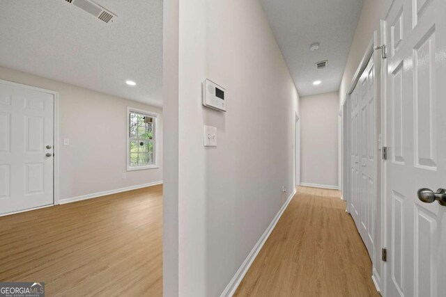 corridor featuring baseboards, light wood-type flooring, visible vents, and a textured ceiling
