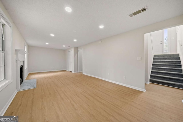 unfurnished living room with stairway, recessed lighting, baseboards, visible vents, and light wood-style flooring