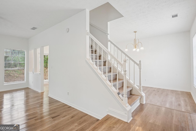 staircase featuring baseboards, visible vents, a chandelier, and wood finished floors