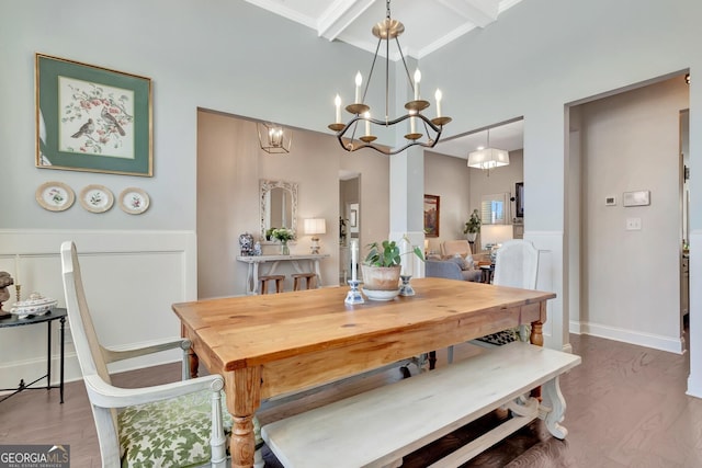 dining area featuring a towering ceiling, beamed ceiling, wood finished floors, and a chandelier