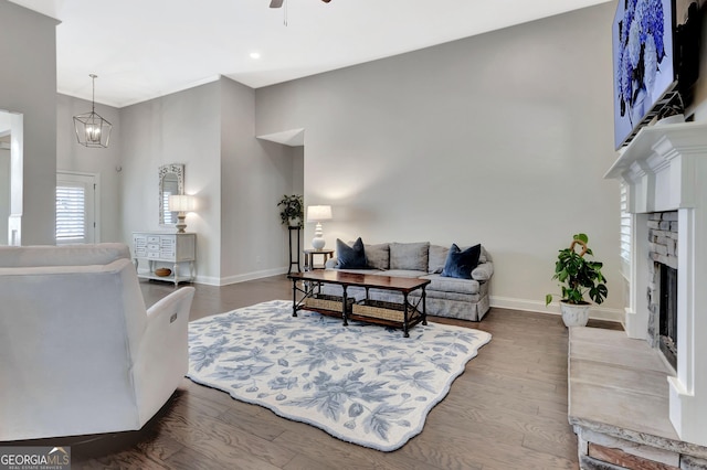 living room with a fireplace, ceiling fan with notable chandelier, baseboards, wood finished floors, and a towering ceiling
