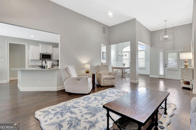living area featuring dark wood-style flooring, an inviting chandelier, baseboards, a towering ceiling, and visible vents