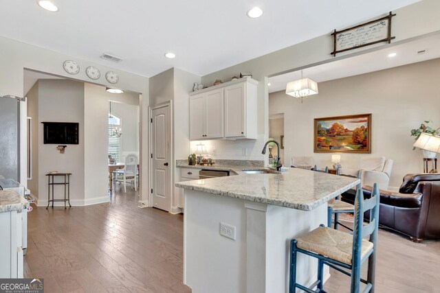 kitchen featuring a breakfast bar area, visible vents, a sink, white cabinets, and a peninsula
